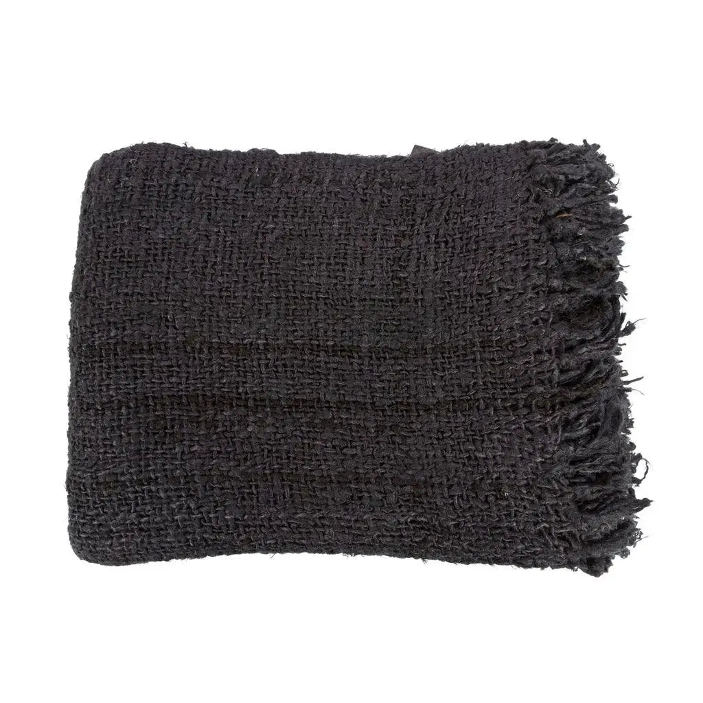 Black cotton throw with a waffle texture and tassels, styled on a rustic wooden chair for a chic and inviting look