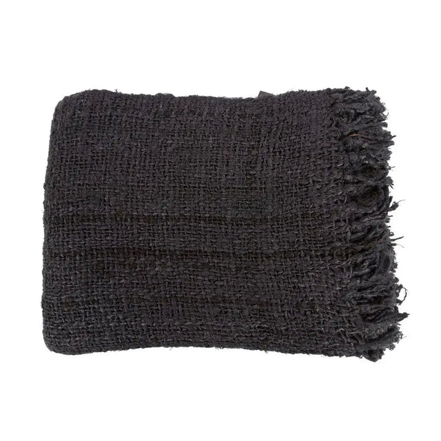 Black cotton throw with a waffle texture and tassels, styled on a rustic wooden chair for a chic and inviting look