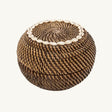 The Colonial Peek-a-Boo Rattan Basket, crafted from durable dark-toned rattan and adorned with elegant cowrie shells, perfect for stylish storage in any room.