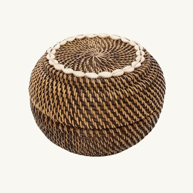 The Colonial Peek-a-Boo Rattan Basket, crafted from durable dark-toned rattan and adorned with elegant cowrie shells, perfect for stylish storage in any room.
