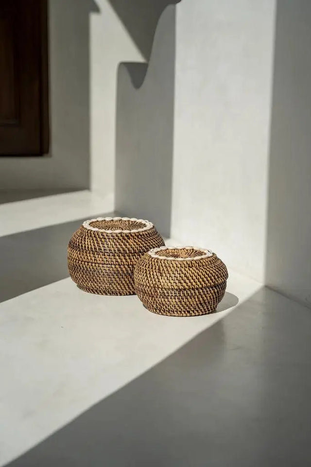 This Colonial Peek-a-Boo Rattan Basket elegantly stores bathroom essentials, adding colonial charm to any space with its dark rattan and cowrie shell accents.