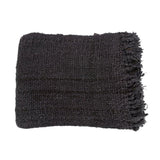 Black cotton throw with a waffle texture and tassels, styled on a rustic wooden chair for a chic and inviting look